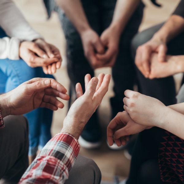 Close-up of hands of people sitting in a circle during a therapy group meeting