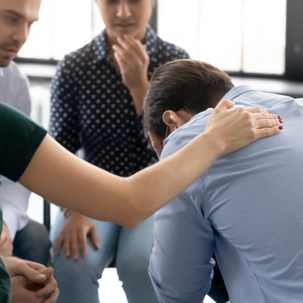 During group therapy session participants supporting crying desperate guy, provide psychological assistance talking encouraging words share mental pain try to help, struggle with addictions treatment